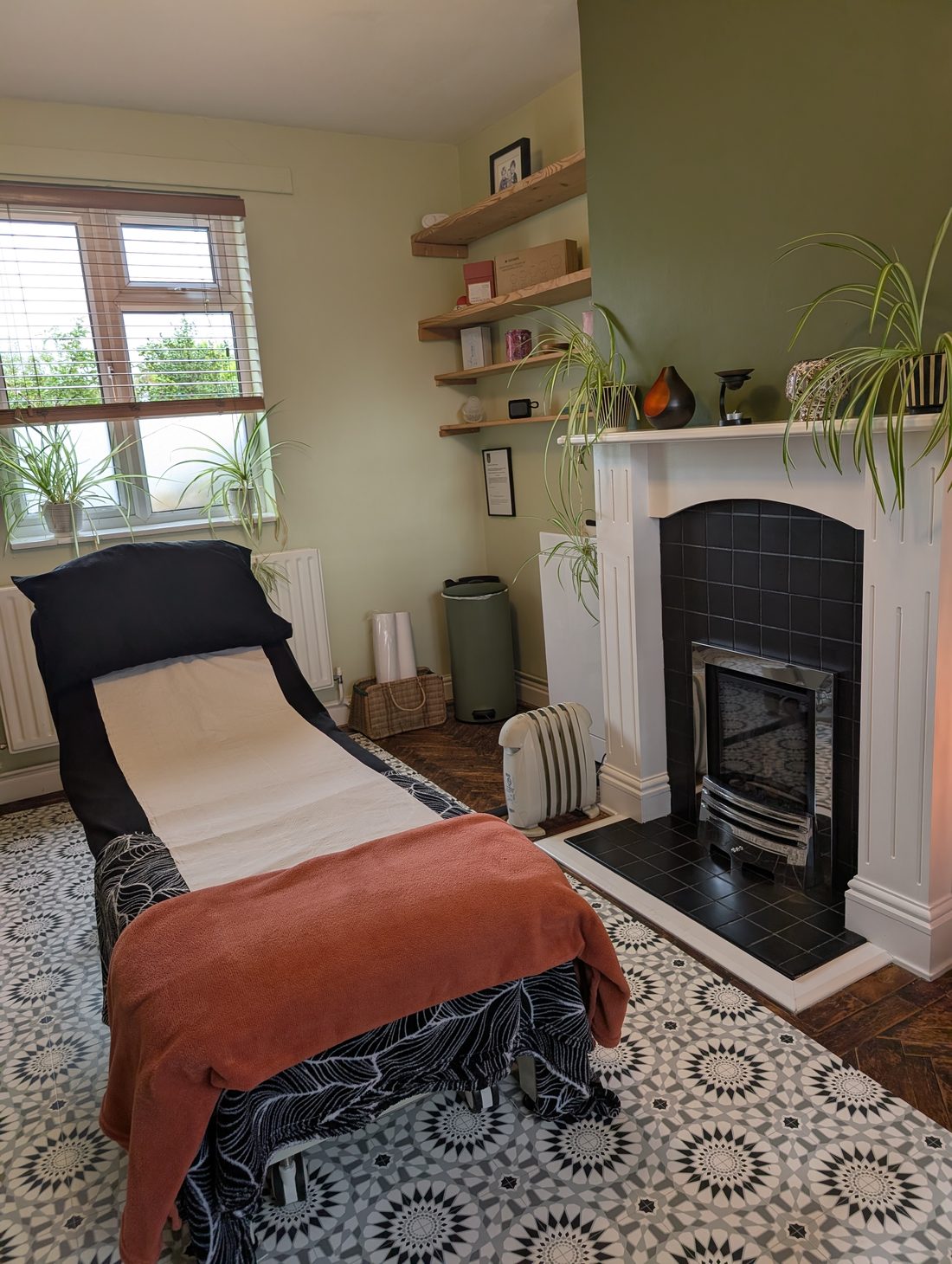 The treatment room: a couch with a copper-coloured blanket beside a white fireplace and patterned tiled floor